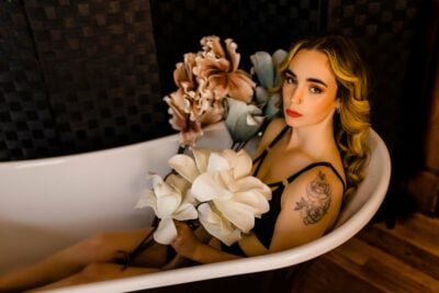 A woman immersed in a bathtub adorned with flowers in a Boudoir Gallery setting.
