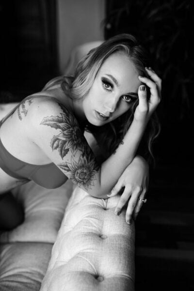 A black and white photo of a woman with tattoos laying on a couch.