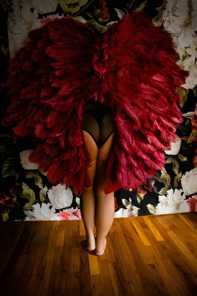 A woman in a red feathered dress posing for a photoshoot in front of a floral wall.