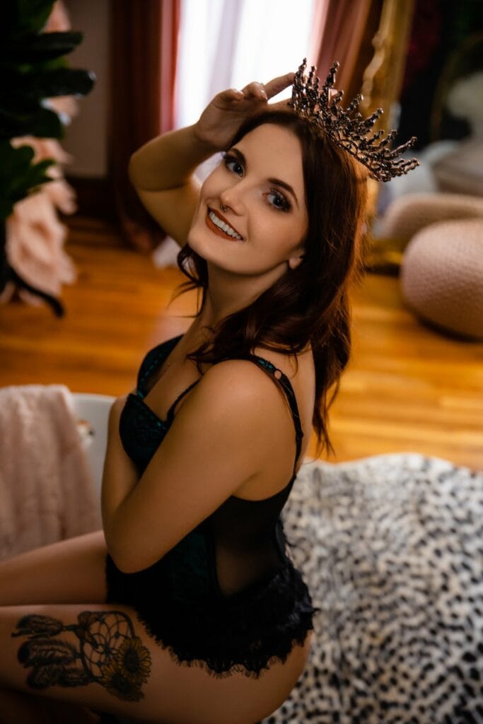 A woman wearing a tiara posing on a leopard print rug for a boudoir photography session.