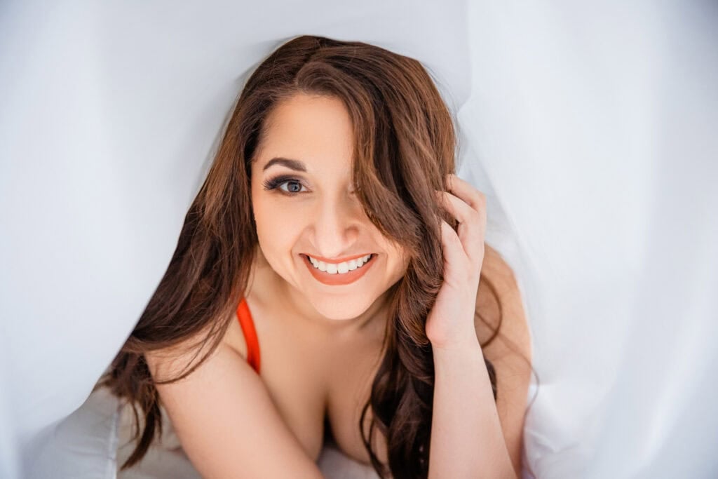 A woman laying under a sheet with a smile on her face.