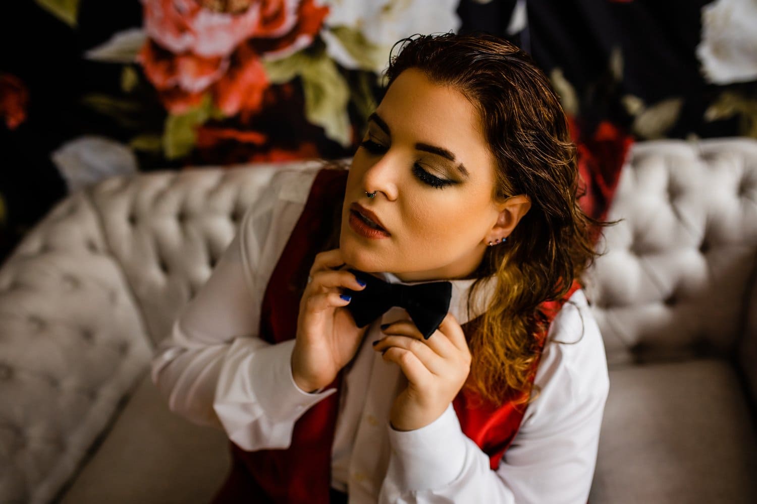 A woman adjusting her bow tie on a couch for a photoshoot.