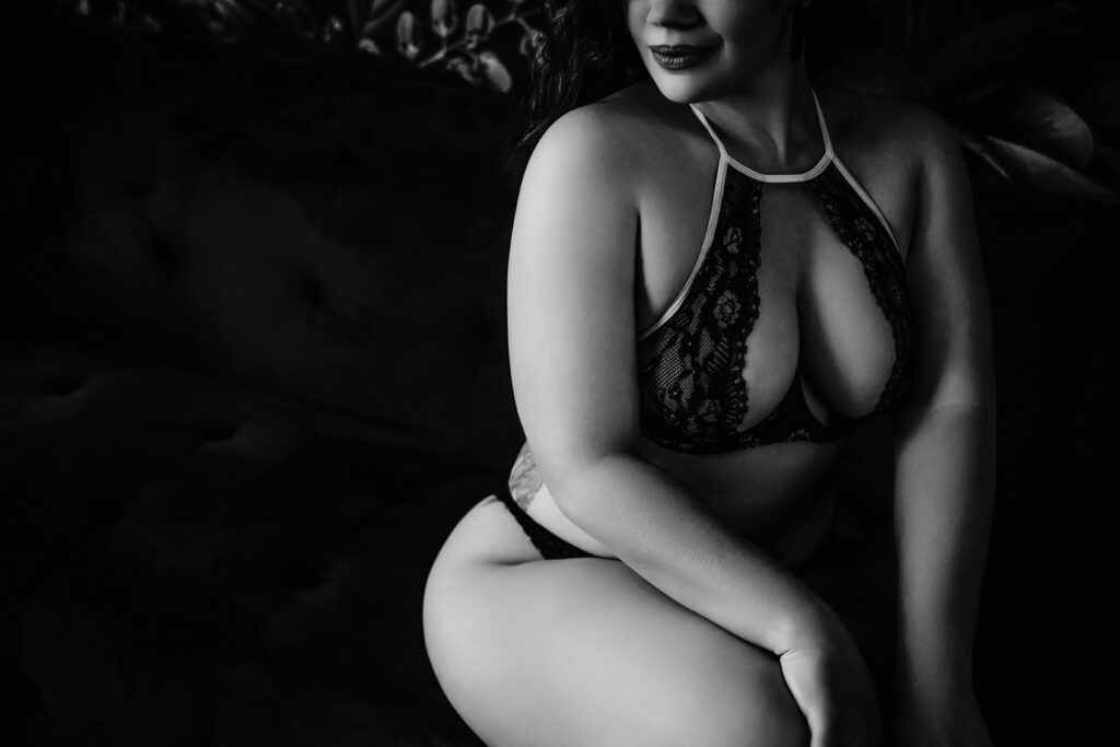 A black and white photo of a woman in lingerie sitting on a couch.